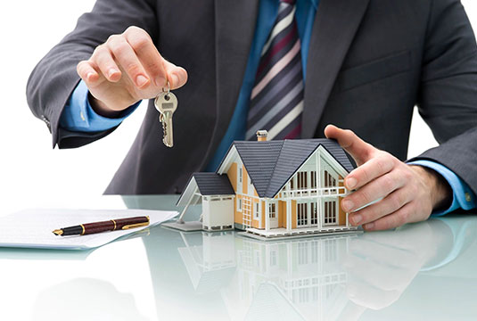 A man in a suit holding out keys to a house.